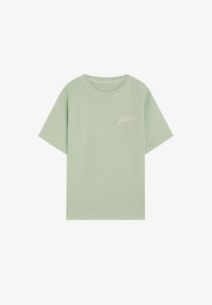 T-shirt vert clair à manches courtes et col rond, avec un petit texte beige « California Aloha » sur le haut gauche de la poitrine.