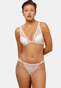 Ensemble de lingerie en dentelle blanche comprenant un soutien-gorge à décolleté plongeant et un string assorti, avec des motifs floraux complexes et des bords festonnés. Texture en dentelle légère.