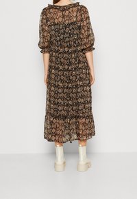 Robe noire longue et fluide avec un motif floral, tissu transparent, manches bouffantes et un ourlet à volants. Associée à des bottes blanches à talons épais.