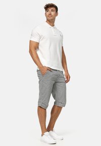 Weißes Polo-Shirt mit kurzen Ärmeln, graue karierte Shorts und weiße Sneaker. Das Outfit hat ein dezentes Logo auf dem Polo und umgeschlagene Shorts-Ärmel.