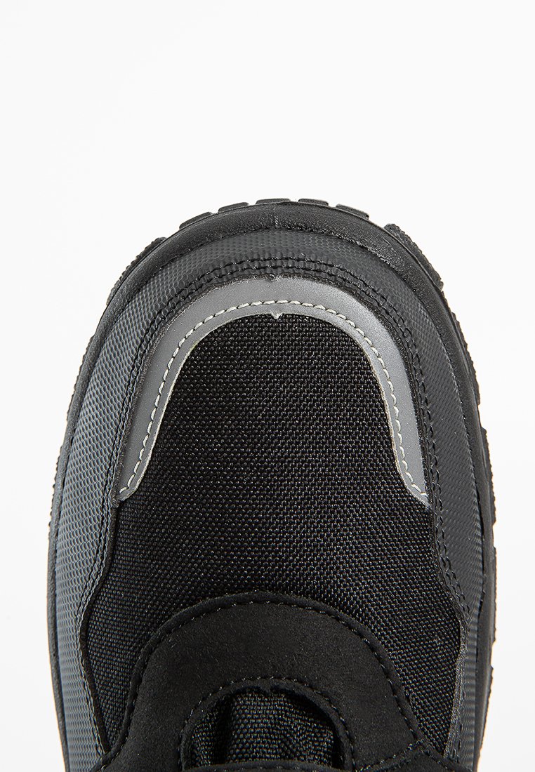 Schwarzer Schuh mit einer strukturierten Oberseite, ausgestattet mit einer verstärkten Zehenkappe und grauen Akzenten entlang des Randes. Die Sohle hat ein robustes Profil.