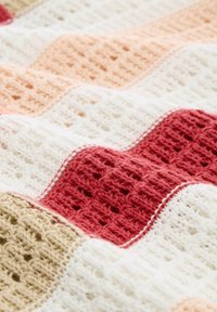 Tissu tricoté rayé avec un motif ondulé texturé en beige, blanc, pêche et rouge.