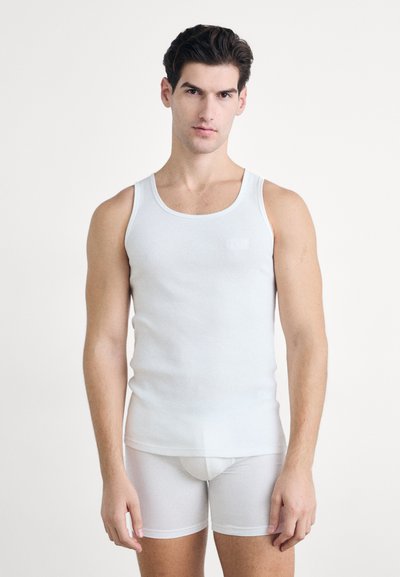Débardeur en coton blanc avec une texture côtelée et des larges bretelles, associé à un sous-vêtement blanc de style brief. Design épuré et minimaliste.