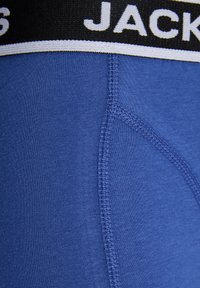 Tanga de homem em algodão azul com uma cintura preta apresentando texto branco "JACK". Detalhes de costura e textura suave.