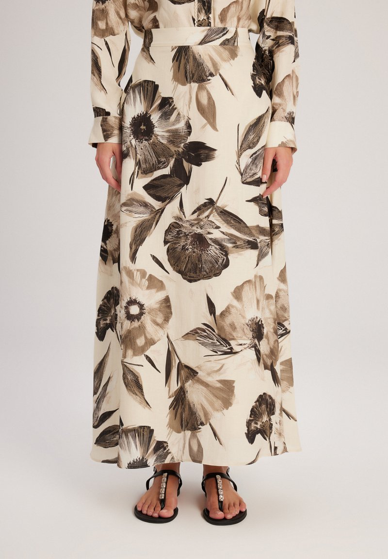 Jupe maxi avec un motif floral dans des tons bruns et beiges, avec une taille ajustée et un tissu fluide. Associée à des sandales plates noires.