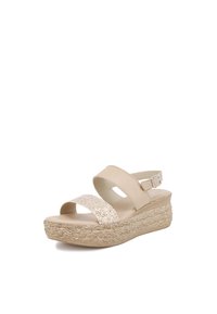 Sandalo con zeppa beige, dotato di due cinturini larghi; uno di essi presenta un accento scintillante. La suola in fibra naturale aggiunge texture. Cinturino regolabile alla caviglia.