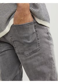Jeans de mezclilla gris con una textura desvanecida y bolsillos sutilmente delineados. La cinturilla está parcialmente cubierta por una blusa de patrón a rayas.