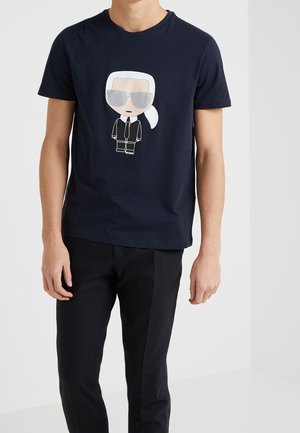 Navy cotton t-shirt featuring a cartoon design of a figure with white hair and sunglasses, printed in light colors, paired with black pants.