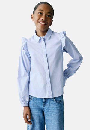 Chemise rayée bleu clair avec des accents de manches froncées, devant à boutons et manches longues. Associée à un jean en denim bleu clair.