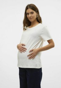Graviditet t-shirt i blød hvid bomuld, korte ærmer, rund halsudskæring, løs pasform, båret over en markant babybuge, parret med mørke jeans.