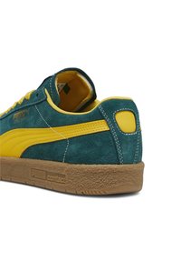 Green and yellow Puma suede sneaker with gum rubber sole, yellow stripe on side, and yellow interior lining.