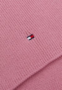 Rosa strikket tekstil med ribbestruktur. Har et lite, brodert logo med røde, hvite og blå striper.