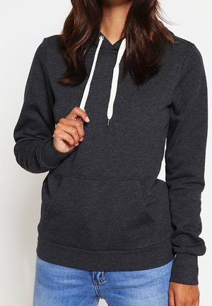 Persoon die een donkergrijze hoodie met witte trekkoorden en een blauwe spijkerbroek draagt, en een trekkoord bij de nek vasthoudt.