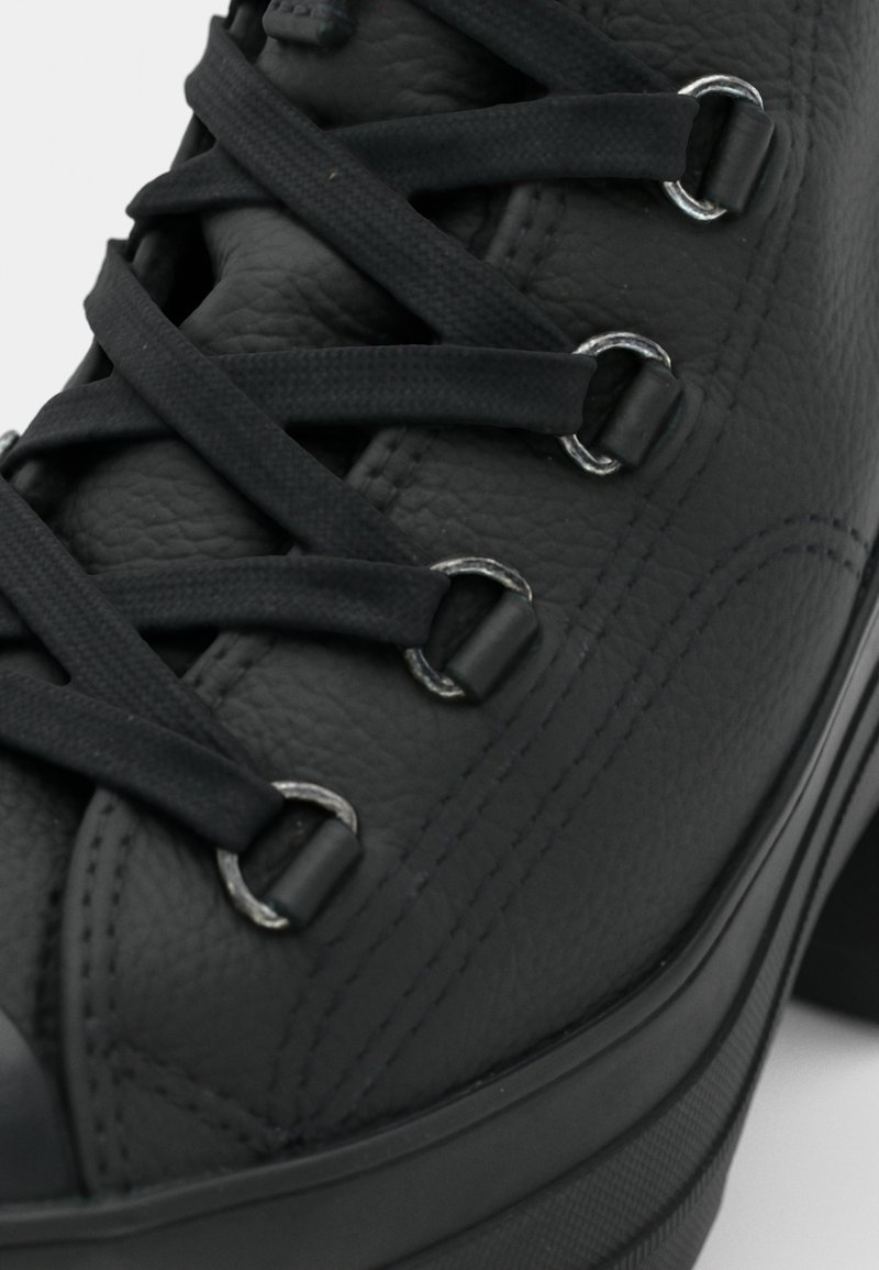 Baskets montantes en cuir noir avec bout rond, lacets noirs, œillets argentés et surface texturée. Accents cousus le long des côtés.
