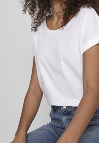 T-shirt blanc à manches courtes avec un col rond, fabriqué en tissu de coton doux. Pantalon en denim bleu taille haute avec fermeture bouton.