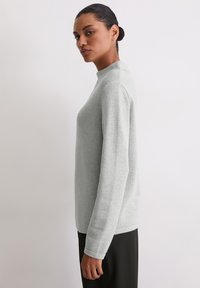 Jasnoszary prążkowany sweter z wysokim kołnierzem, długimi rękawami i gładką fakturą. W zestawieniu z czarnymi, luźnymi spodniami dla kontrastu.