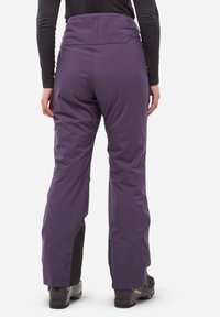 Pantalons de ski violets en tissu résistant à l'eau, avec une taille haute et des accents noirs renforcés aux chevilles.