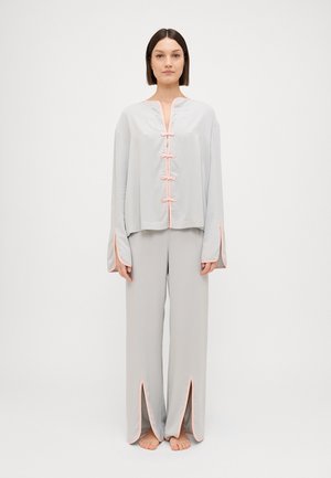 Set di pigiama grigio chiaro composto da una maglietta a maniche lunghe con rifiniture rosa e chiusure a gancio, abbinato a pantaloni coordinati con spacchi all'orlo.