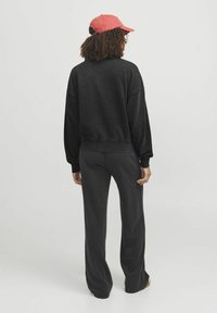 Sudadera negra con hombros caídos y puños acanalados, combinada con pantalones oscuros de pierna ancha. El modelo lleva una gorra roja. Tejido suave y casual.