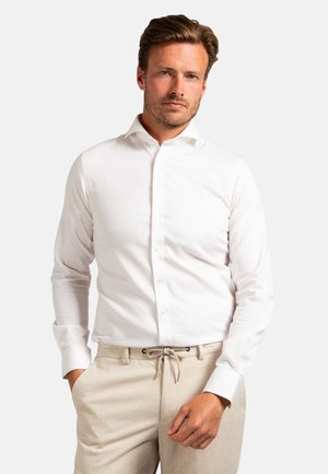 White button-up shirt with a collared neckline and long sleeves, worn over beige textured pants with drawstring. Smooth fabric, tailored fit.