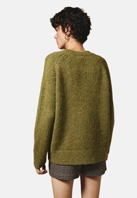 Olijfgroen gebreide trui met een relaxte pasvorm, ronde hals en geribbelde zoom. Getextureerde stof met een zachte, iets flonkerende uitstraling.