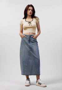 Kuttet kremfarget ribbestrikket topp med svart kant, høyt liv blå denimskjørt med frontsømdetaljer, sammen med hvite sneakers med svarte detaljer.