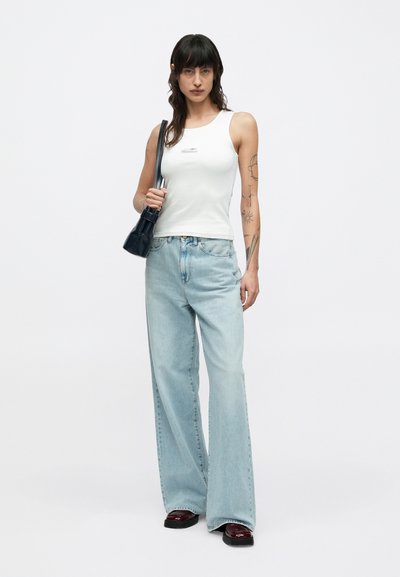 Λευκό μπλουζάκι χωρίς μανίκια, ανοιχτό μπλε τζιν φαρδύ, μαύρη τσάντα χειρός και σκούρα κόκκινα παπούτσια. Μινιμαλιστικός σχεδιασμός και άνετη, καθημερινή εφαρμογή.