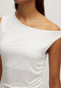 Witte, een-schoudertop van zacht materiaal met een getailleerd ontwerp. Heeft zijwaartse rimpelingen voor textuur en een soepele, gedrapeerde uitstraling.