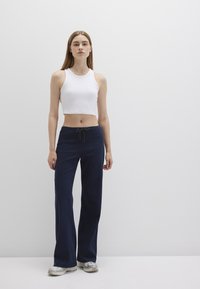 White ribbed crop top paired with navy wide-leg pants featuring a drawstring. The model wears metallic sneakers. Plain background.