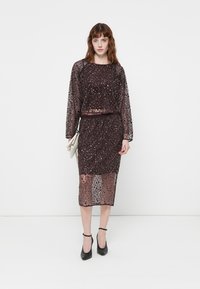 Luxe sequined top en rokset in donker bourgondisch, met een doorzichtige overlay. De jurk heeft een rechte snit met een knie-lange zoom.