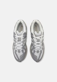 Szare i białe buty sportowe wykonane z siateczki i materiałów syntetycznych, z systemem sznurowania, wyściełanym kołnierzem oraz teksturowaną podeszwą.