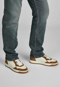 Weiße und braune Sneaker aus Wildleder und Leder. Niedriges Design mit perforierten Details, Schnürsenkeln und einer Gummisohle.