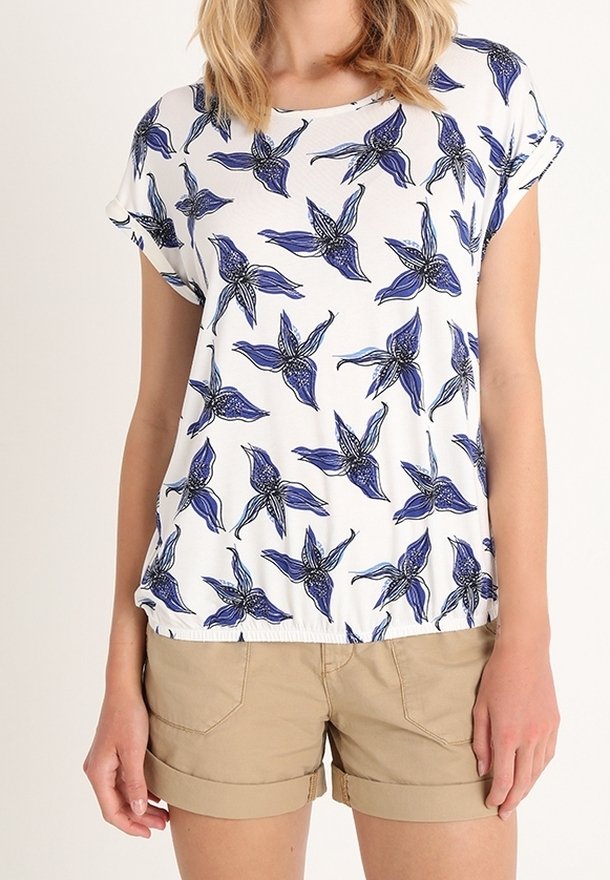 T-shirt blanc avec motif floral bleu, manches courtes et encolure ronde. Associé à un short beige, ourlet visible et légère fronce à la taille.