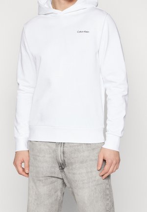 Sudadera blanca hecha de tela suave, con bolsillo canguro, puños acanalados y un pequeño logo negro de Calvin Klein en el pecho.