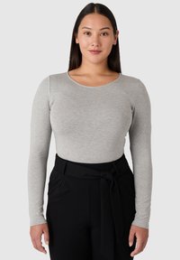 Dlouhý rukáv, tričko s kulatým výstřihem v světle šedé tkanině, s hladkou texturou a přiléhavým střihem, spárované s černými kalhotami s vysokým pasem.
