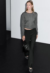Gray long-sleeve cropped sweater, black tailored pants, gray heels, and a black handbag. Clean lines and modern silhouette against a minimal backdrop.