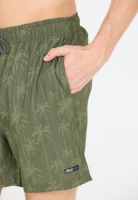 Olivgröna badshorts med ett palmträdsmönster, elastisk midja och sidoficka. Har en liten varumärkesetikett vid fållen.