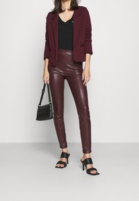 Burgundy textured blazer över en svart topp, kombinerad med högmidjade burgundy faux läderbyxor och svarta sandaletter med klack. Bär en svart handväska.