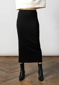 Sort, knælang nederdel lavet af strækbart stof med en tætsiddende pasform. Parret med sorte stilethæl ankelstøvler. Enkel, slank fremtoning.