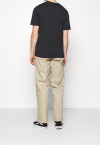 Schwarzes Baumwoll-T-Shirt, beige lockere Hose und schwarze Sneakers. Die Hose hat eine Seitentasche und ein kleines Etikett. Einfaches, lässiges Design.