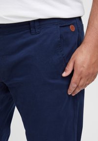 Pantalone mornarske plave boje od pamuka, s glatkom teksturom, džepom na dugme s kožnim akcentom i ravnim krojem.