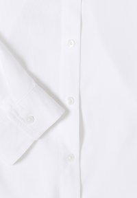Chemise en coton blanc à manches longues, avec un poignet détaillé doté d’un bouton, et une rangée verticale de boutons blancs sur la patte de boutonnage avant.
