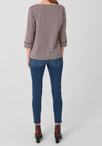 Blusa a rayas en rojo y blanco con mangas tres cuartos. Combinada con jeans ajustados azules y botas de tobillo con tacón grueso.