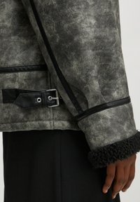 Graue Kunstlederjacke mit strukturiertem Finish, ausgestattet mit einem schwarzen Kunstfellbund, schwarzen Akzenten und einem silbernen Schnallendetail.