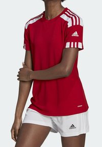 Czerwona sportowa koszulka z białymi paskami na ramionach i logo Adidas; krótki rękaw, okrągły dekolt, wykonana z materiału odprowadzającego wilgoć. Połączona z białymi szortami.