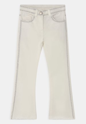 Beige flared jeans with contrast stitching, front pockets, and studded accents along the sides; raw hem at the bottom.