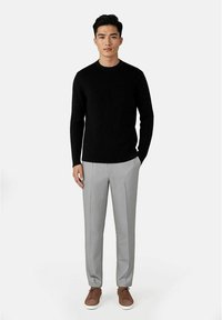 Svart ribbet genser kombinert med lysegrå dressbukser og brune sneakers. Antrekket har en tettsittende silhuett og lange ermer.