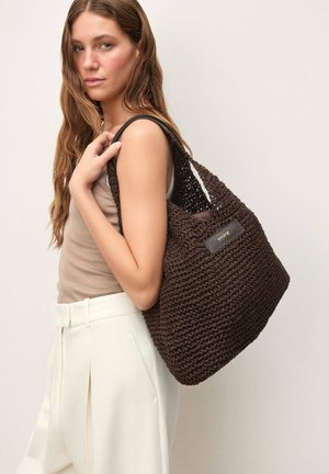 Rjava pletena torbica z mehkim, teksturiranim zaključkom, z ozkimi ramenskimi trakovi in usnjenim poudarkom na etiketi. Velik, sproščen dizajn.