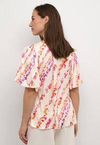 Blusa a maniche corte in crema chiaro, con motivi astratti colorati in rosa, arancione e viola; tessuto morbido con una vestibilità rilassata.