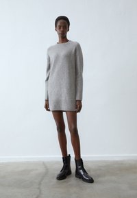 Vestido de suéter gris de punto con dobladillo acanalado, con mangas largas y cuello redondo, combinado con botas de tobillo negras con cordones.